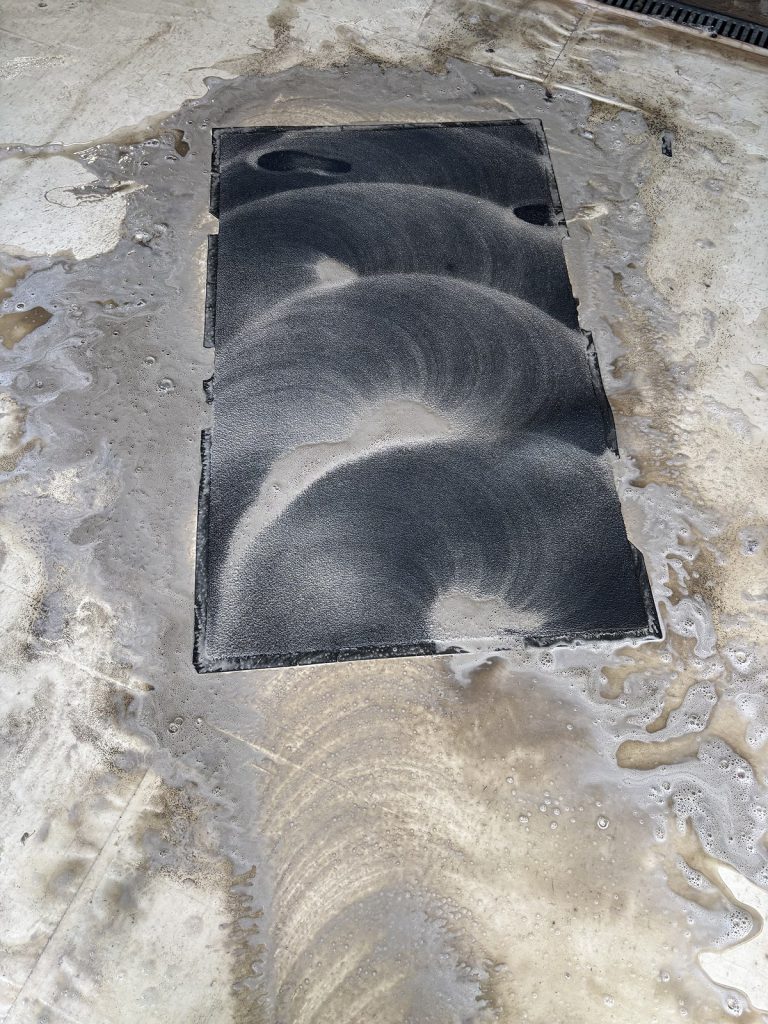 Pranie ciemnego dywanu z użyciem piany podczas procesu czyszczenia w pralni Dywanik